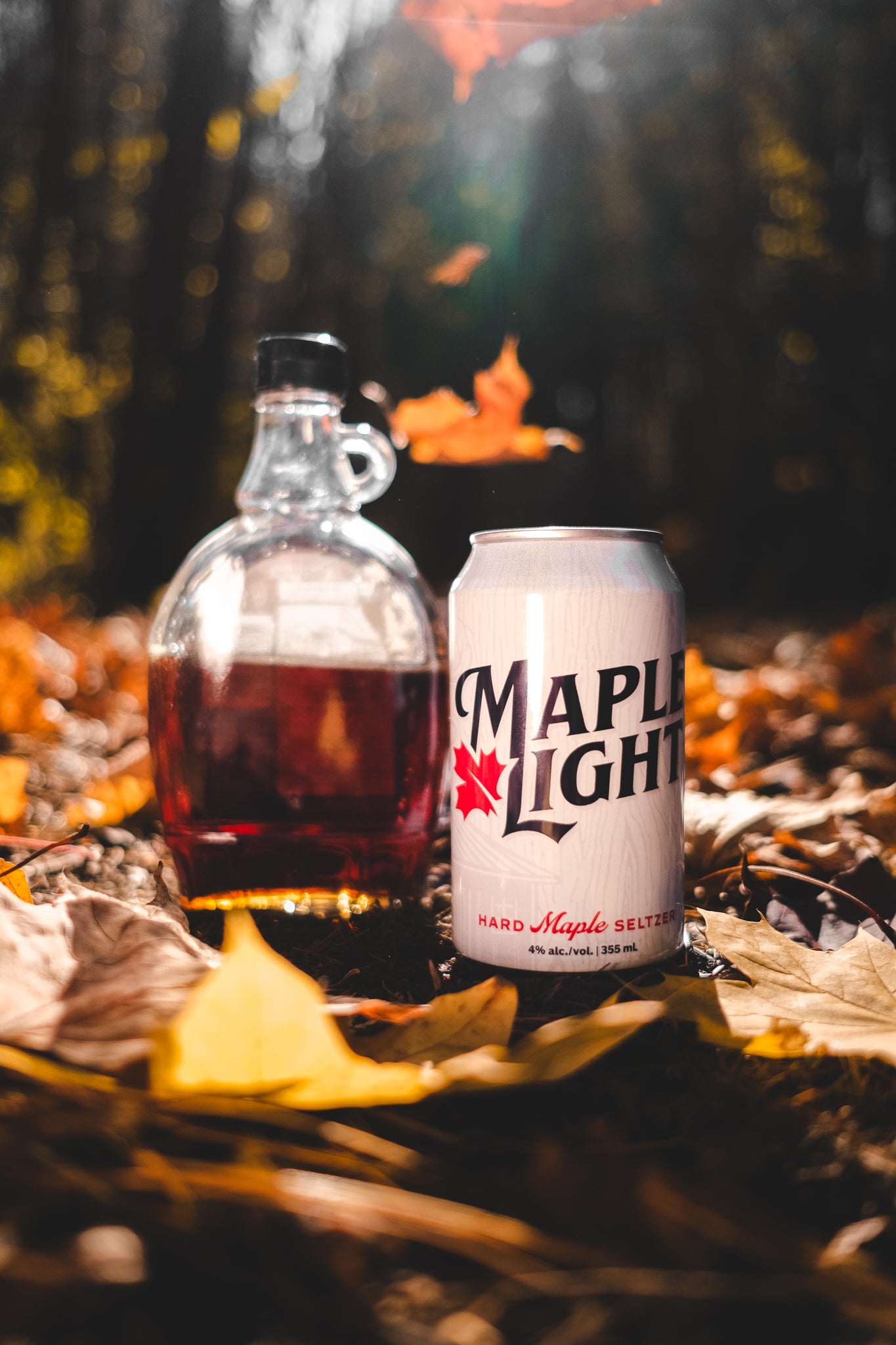 A can of Maple Light sitting on pile of maple leaves, with a bottle of maple syrup in the background.